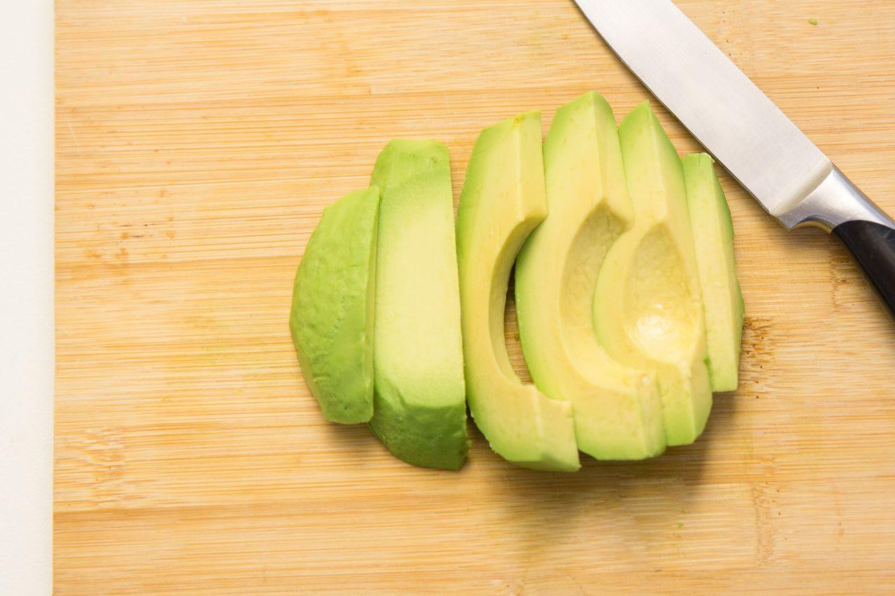 Sliced avocado arranged on a wooden cutting board with a knife placed next to it