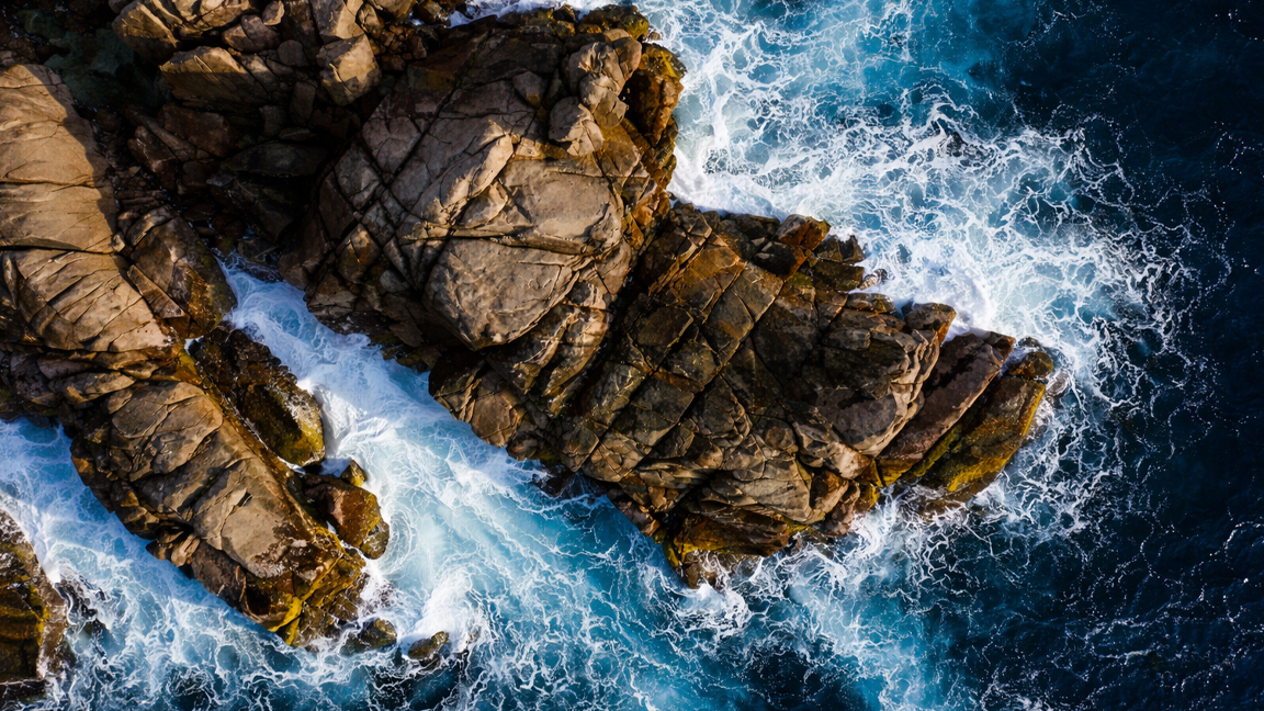 Foamy sea waves surrounding jagged rocks at the shore
