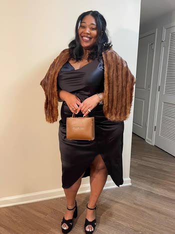 Person smiling in satin wrap dress with fur stole, holding a small handbag