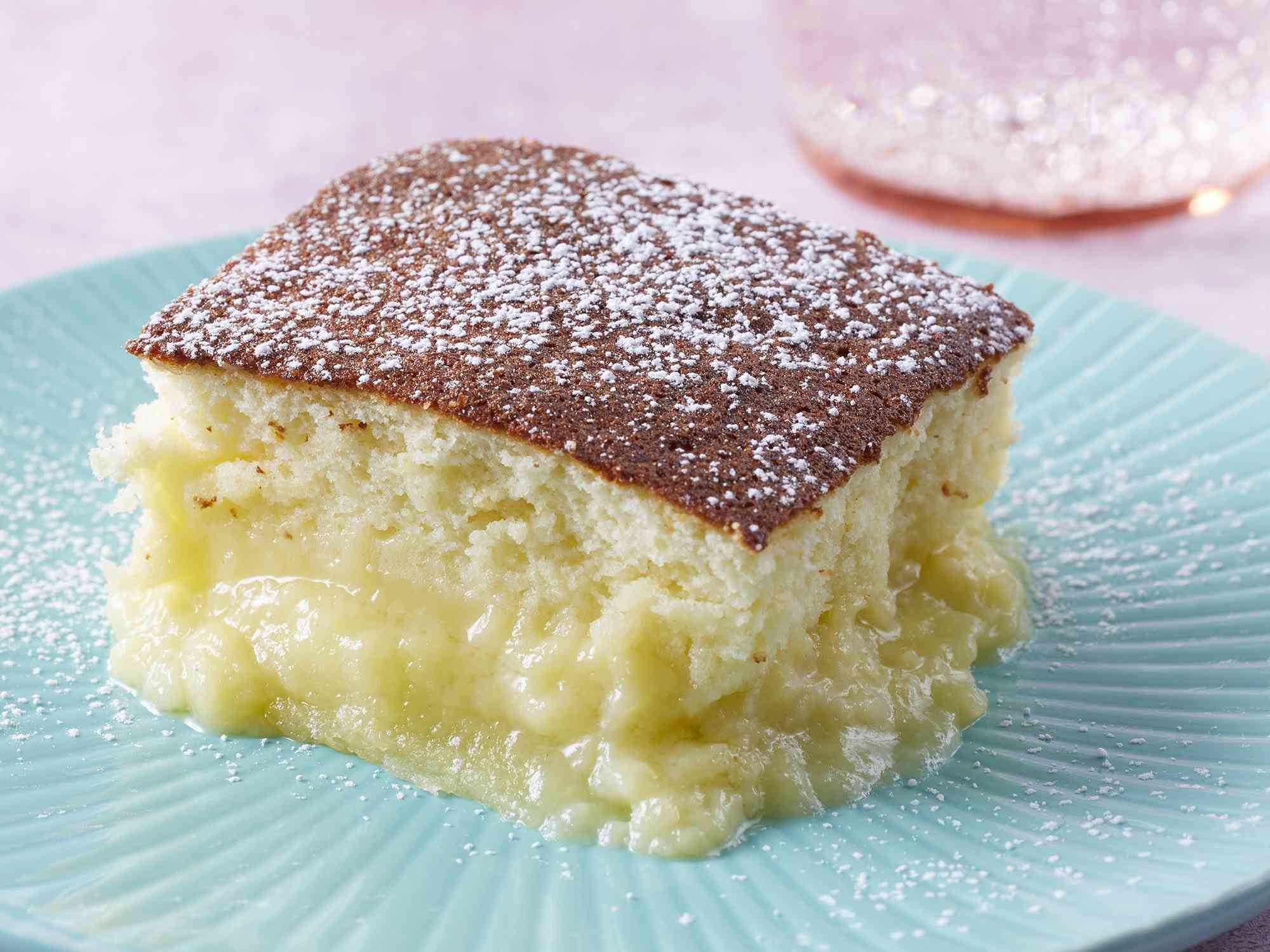 close up on a single slice of lemon pudding cake topped with confectioners' sugar