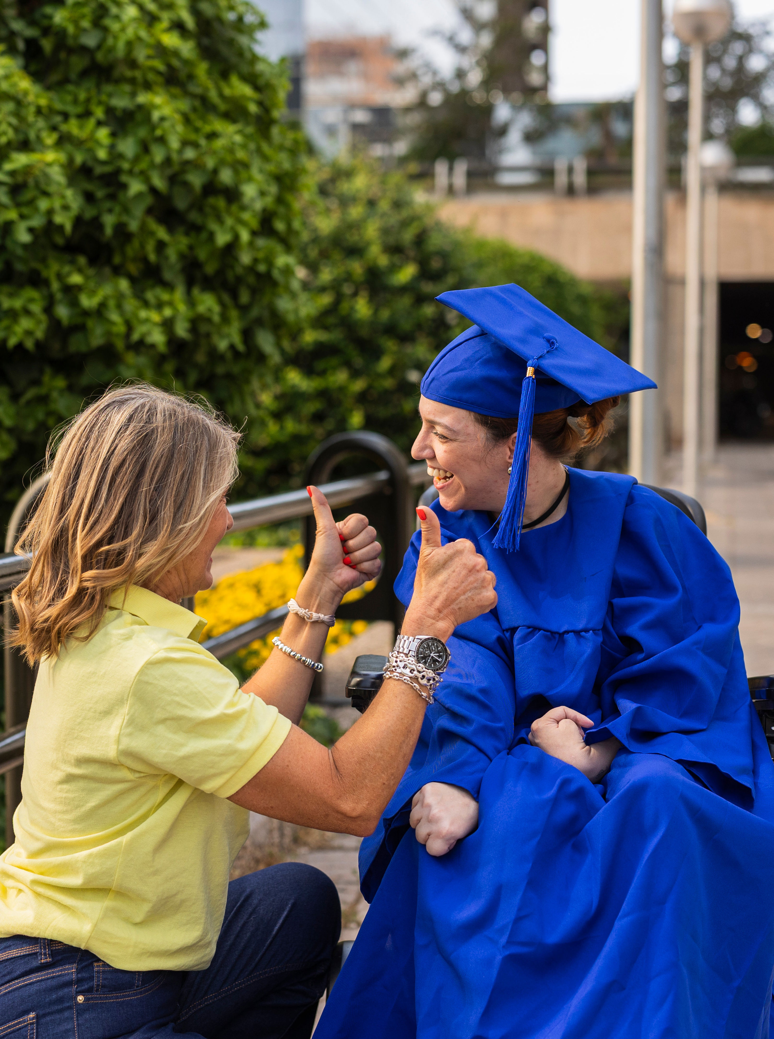 Graduate in a cap and gown shares a joyful moment with a woman giving a thumbs-up, highlighting achievement and support