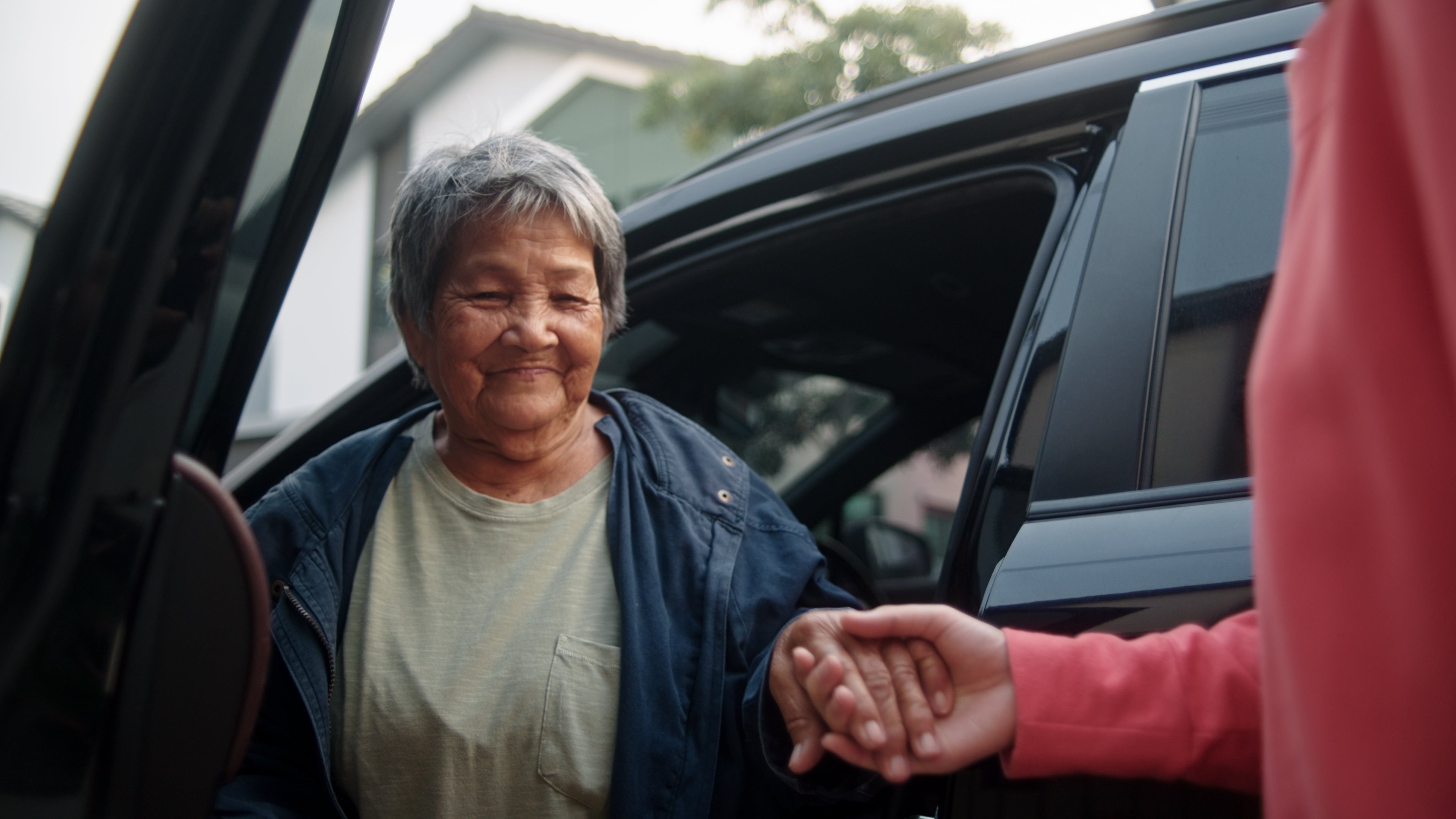 A person helps an elderly woman out of a car, showcasing support and assistance, relevant to work and caregiving themes
