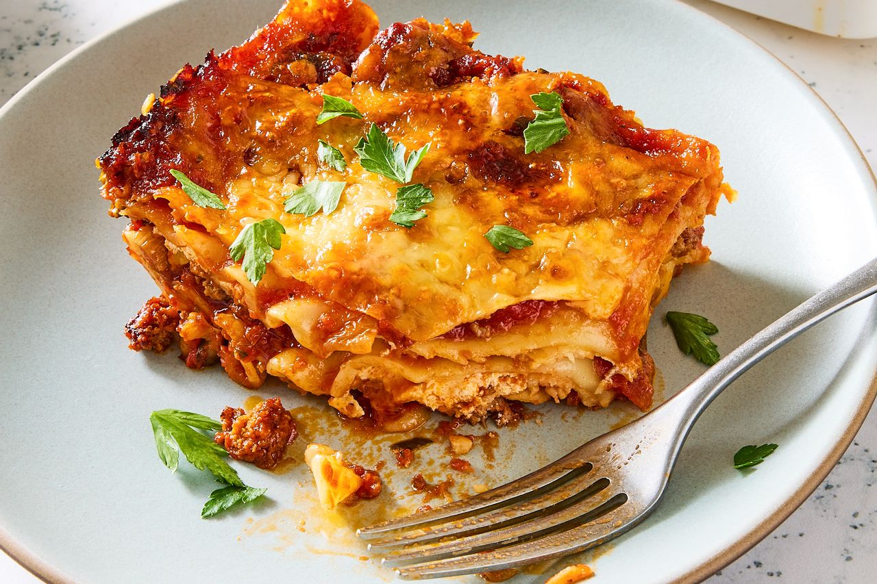 Plated lasagna slice with visible layers of pasta meat and cheese garnished with parsley served on a pale dish with a fork