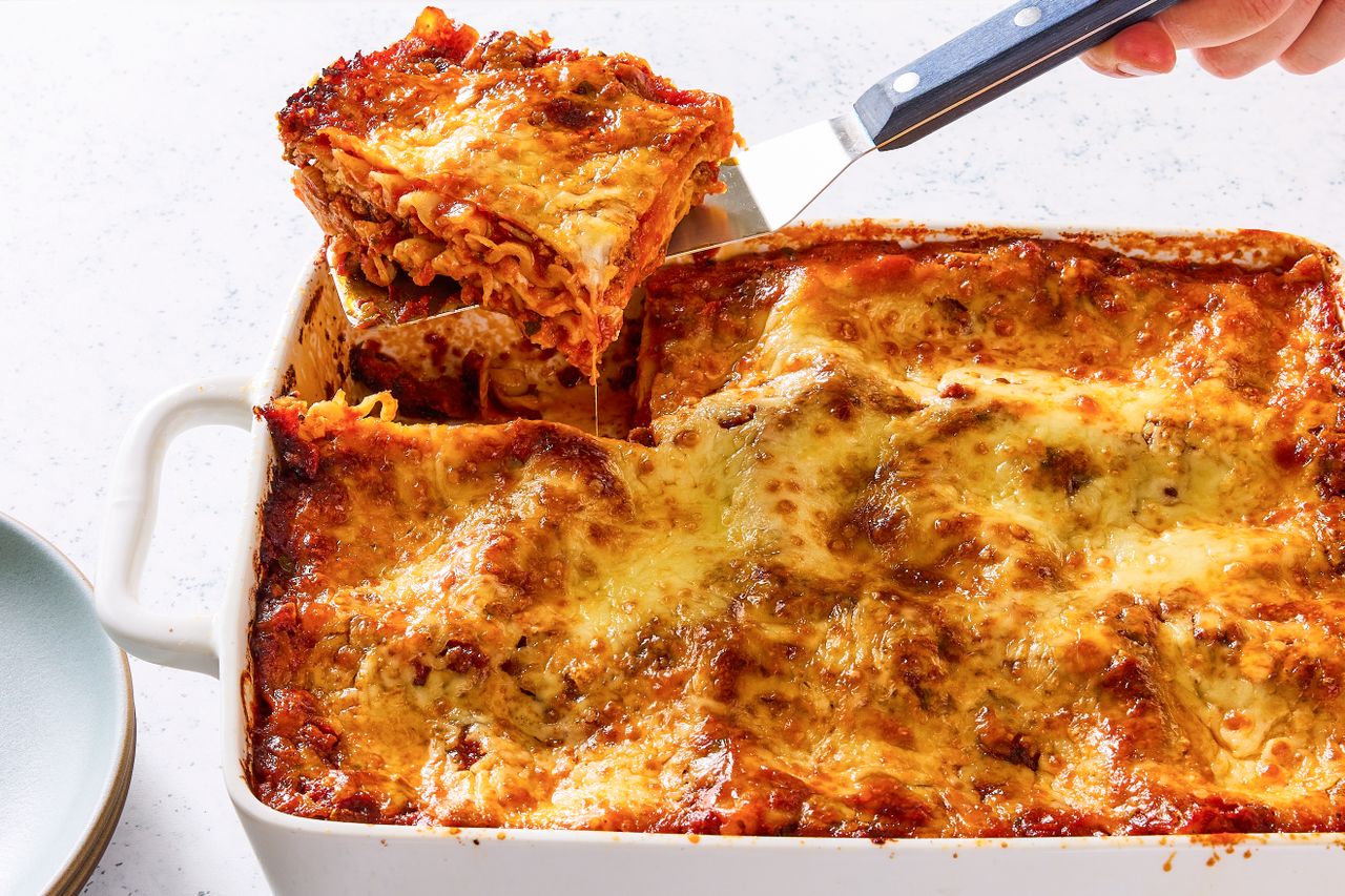 A dish of baked lasagna with a slice being served with a spatula