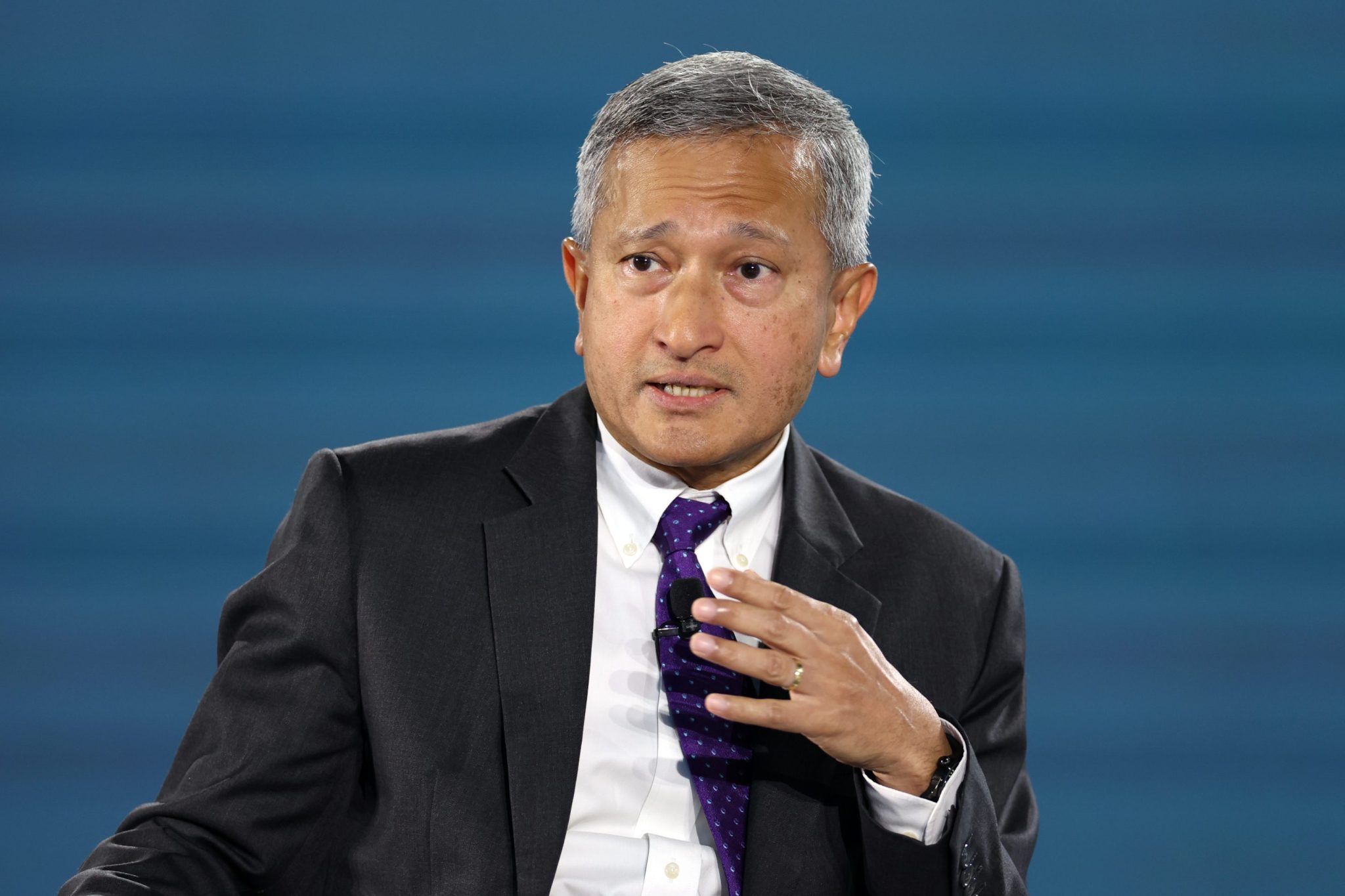 Vivian Balakrishnan, wearing a suit and in front of a blue backdrop, speaks and gestures with his hand.