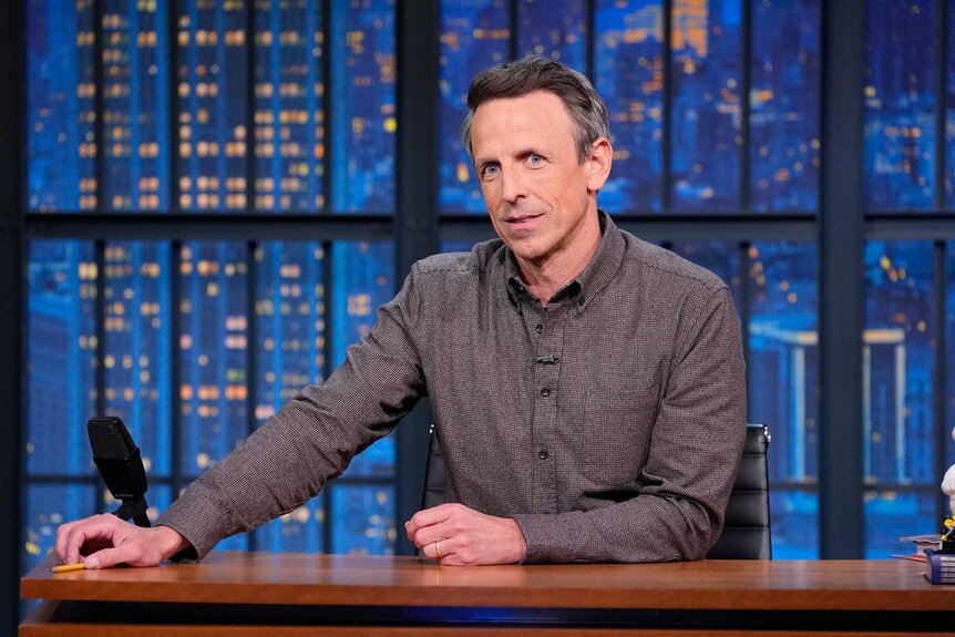 Seth Meyers sitting at a desk during Late Night with Seth Meyers Season 13 Episode 91.