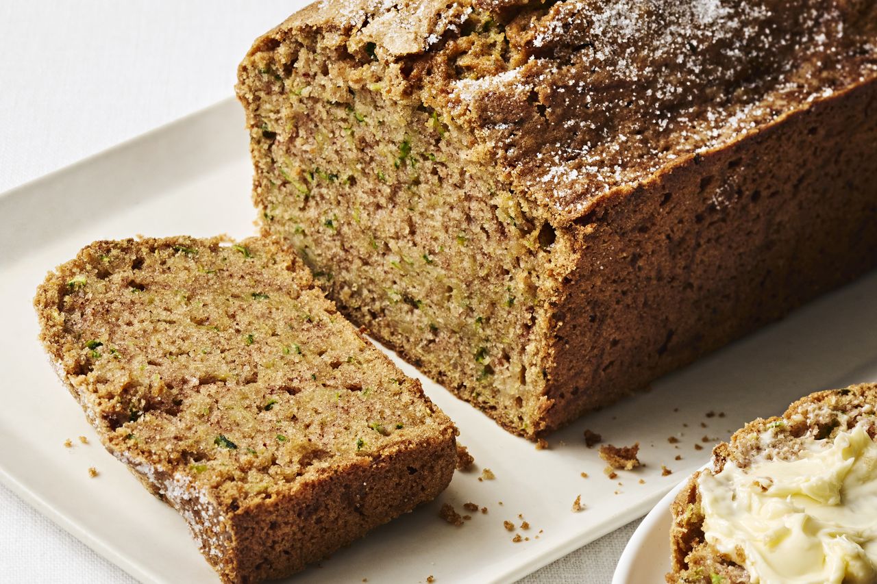 A loaf of zucchini bread with one slice cut off displayed on a white plate
