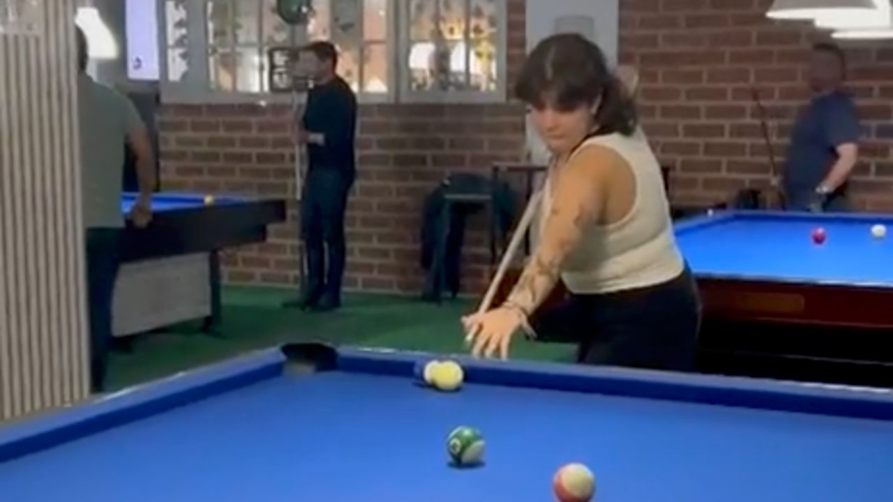 Woman accidentally hits the billiards light while lining up a shot