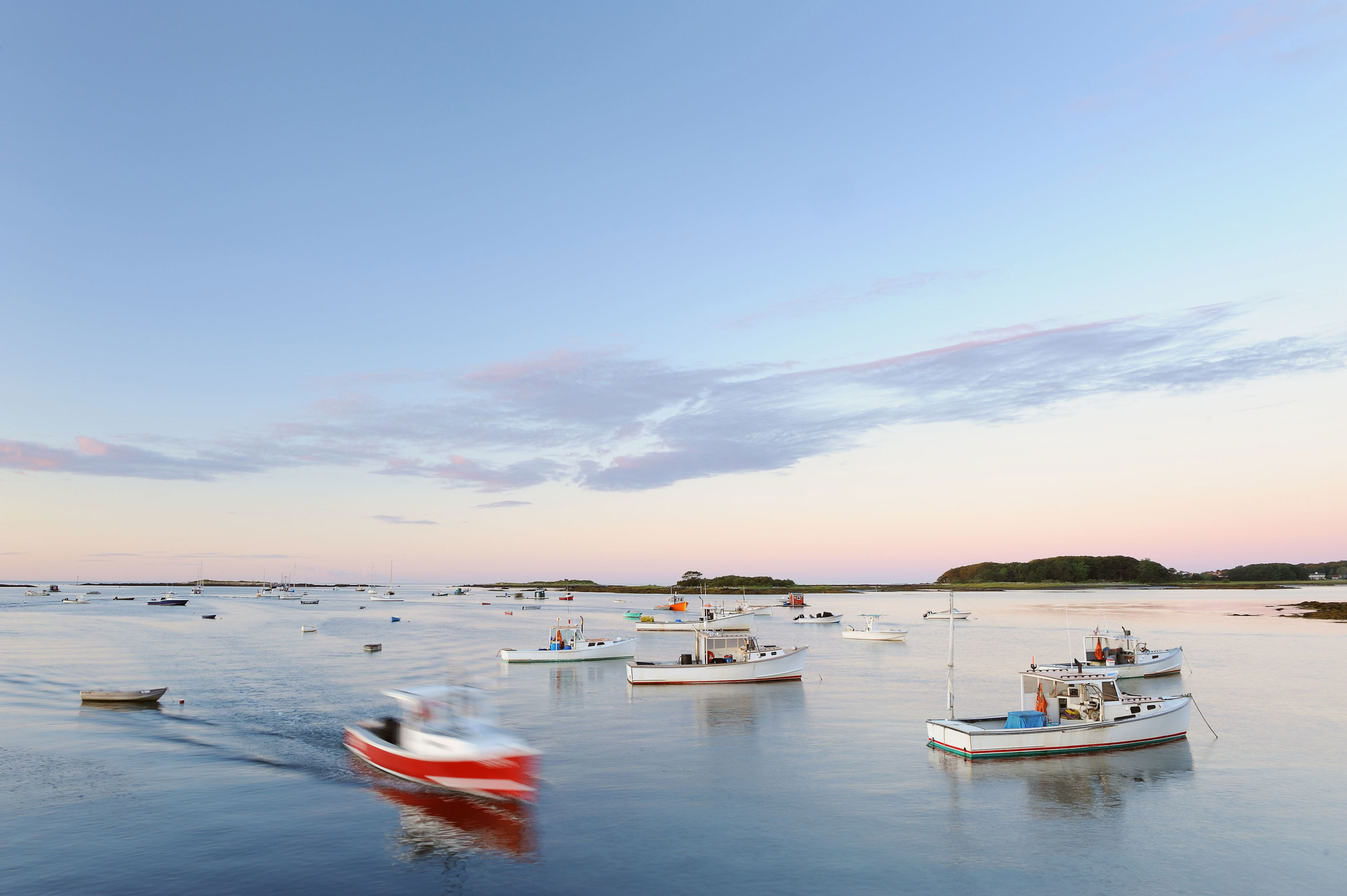 Fishing boats moored in Cape Porpoise harbor at sunrise with boat passing by in blurred motion, Maine, USA