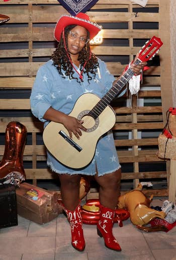 Person in denim dress and red boots poses with guitar at a Western-themed party display with cowboy hats and balloons