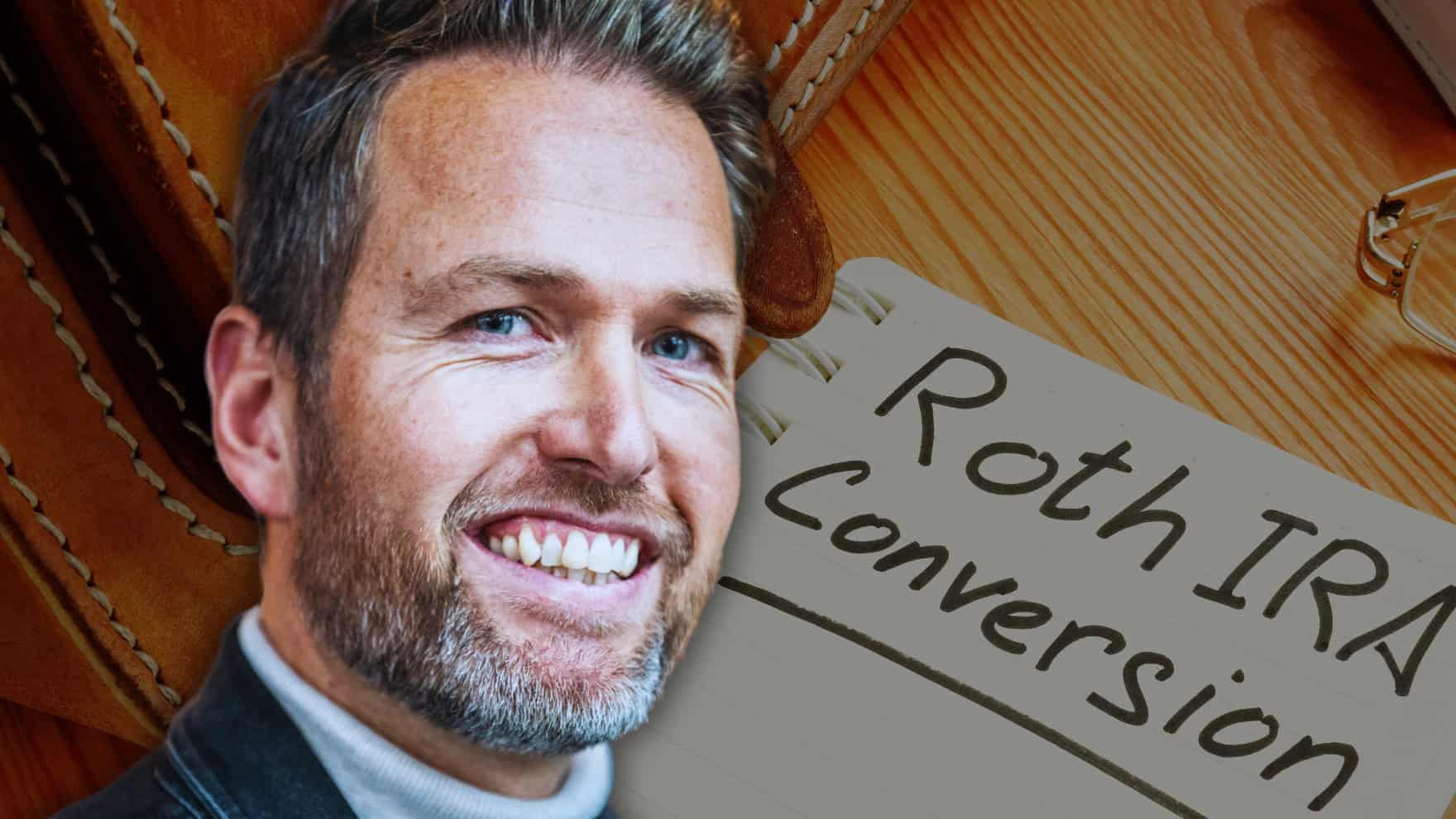 A smiling man with a beard and blue eyes is shown on the left side of the frame, looking towards the right. On the right, a white notebook page with the handwritten words 'Roth IRA Conversion' is visible. The background is a warm, light brown wooden surface with hints of stitched leather.