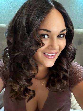 Person with long, curled hair wearing a V-neck top, smiling at the camera
