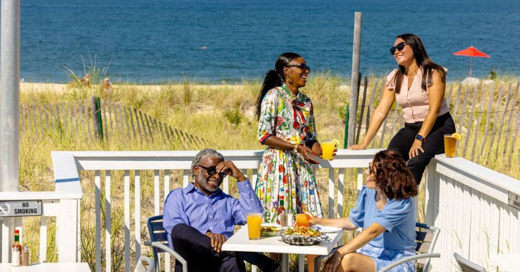 Four people laughing and eating on the Buoy 44 Restaurant Patio in Chic's Beach - Hidden Waterfront Town VA