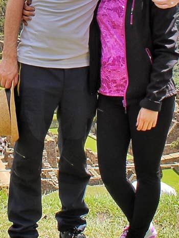Another reviewer's photo of them and their partner standing close, one person in a black shirt and pants, the other in a pink top and black leggings, with the money belt completely hidden and invisible beneath their clothing