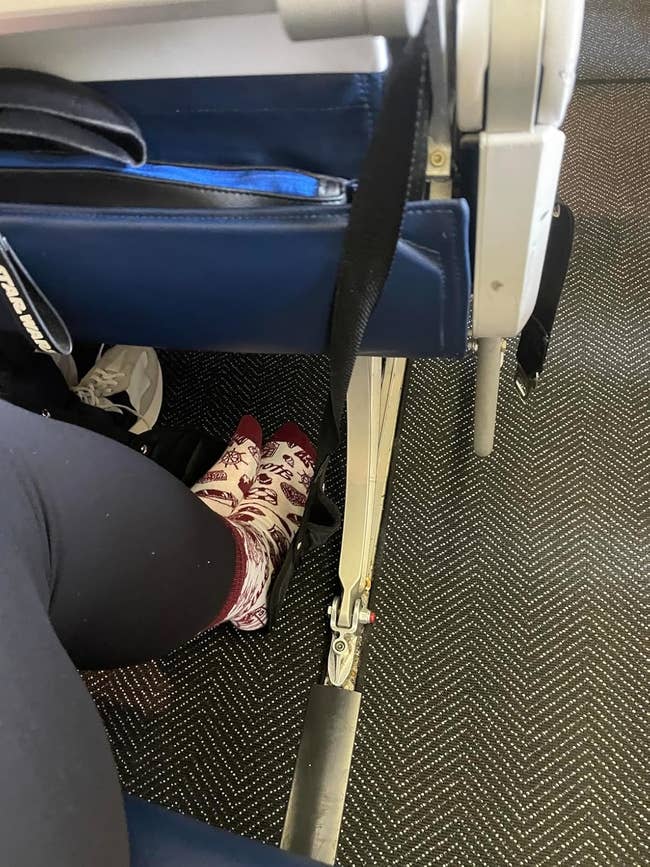 Reviewer's photo of their feet in the foot hammock while seated on an airplane