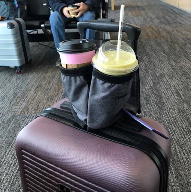 Reviewer's photo of the cup holder in the color Carbon Black, strapped to a purple suitcase and holding two drinks