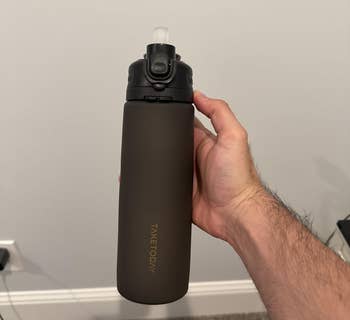 Hand holding a sleek, matte-finish water bottle with a flip-top lid.