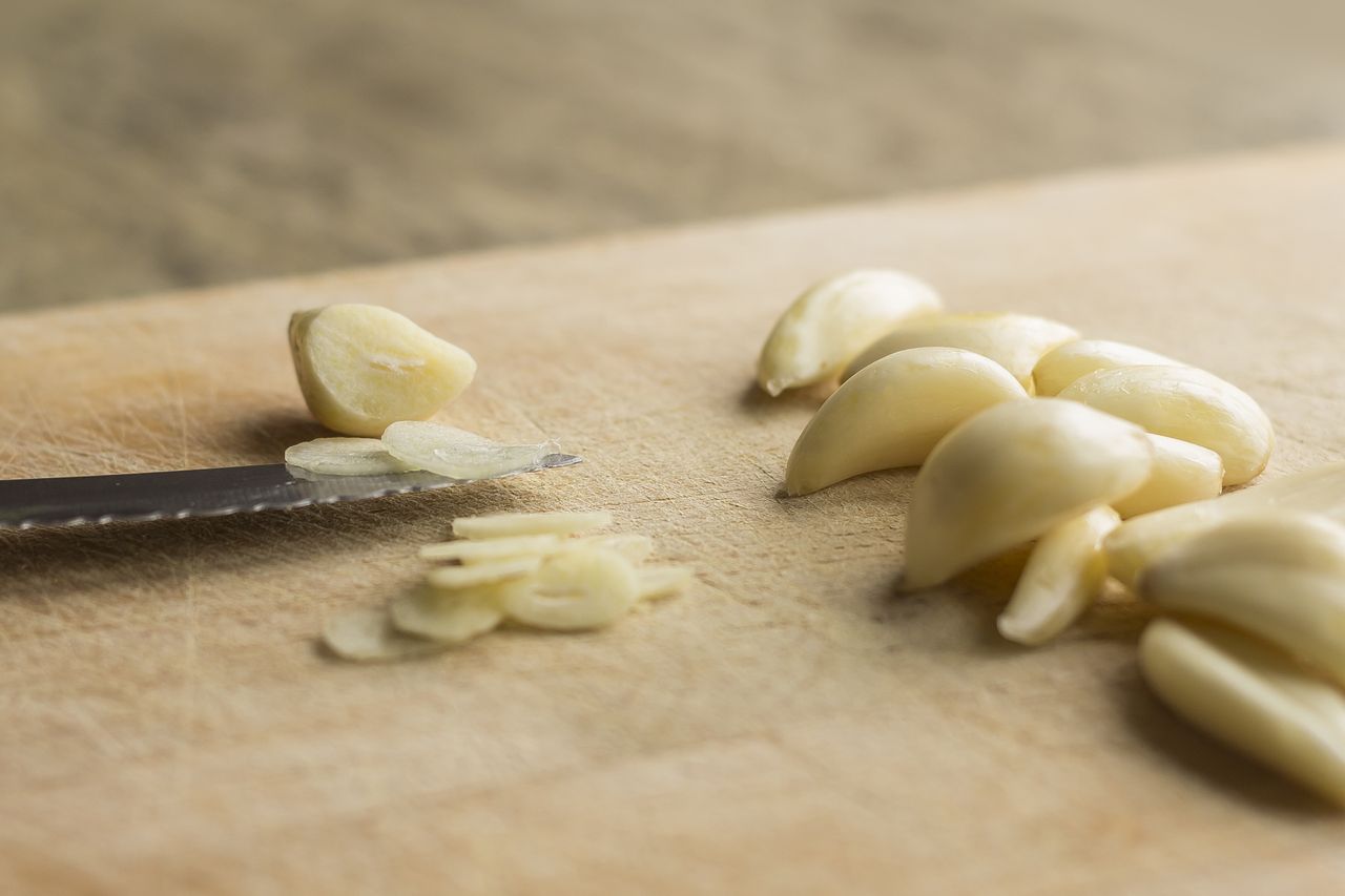 Sliced garlic cloves on a cutting board next to a knife