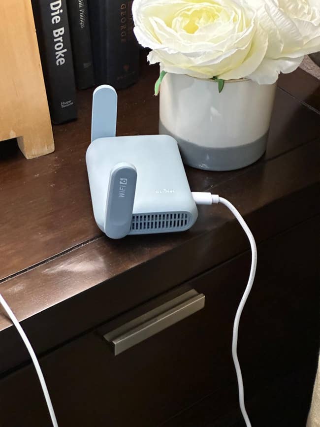 Compact Wi-Fi extender with one antenna on a dresser next to a vase of flowers. Plugged in and ready for use