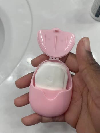 Hand holding a small pink case with open lid, revealing soap sheets inside