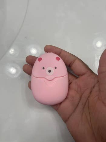 Hand holding a small, bear-shaped pink case used to store soap sheets