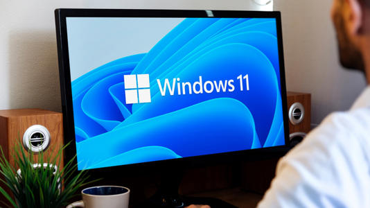 a computer showing the windows 11 logo with a person sitting infront of it