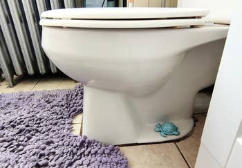 Toilet with a decorative turtle figurine at the base, set on a textured bathroom rug