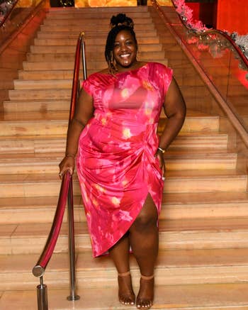 Person in a stylish, fitted dress with a side slit poses confidently on stairs, smiling for the camera