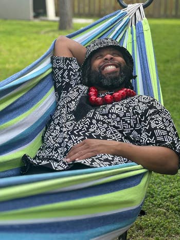 Person relaxing in a hammock, wearing a patterned shirt and bucket hat, with a large beaded necklace. Perfect for outdoor leisure shopping features