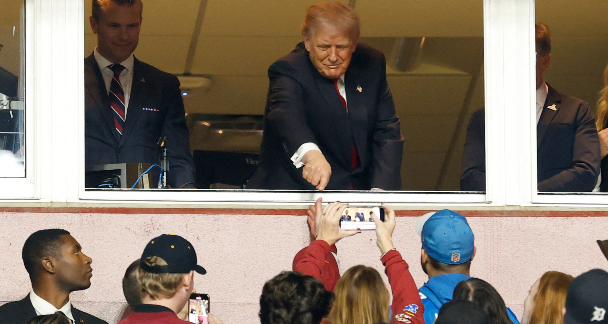 Nov 9, 2025; Landover, Maryland, USA; President Donald Trump gestures to fans while standing next to U.S. Secretary of War Pete Hegseth (L) after swearing in a new group of U.S. military recruits during halftime of the game between the Detroit Lions and Washington Commanders as part of the NFL Salute to Service initiative at Northwest Stadium. Mandatory Credit: Geoff Burke-Imagn Images