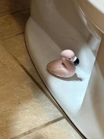 Small flamingo figurine placed on a bathroom floor near the base of a toilet