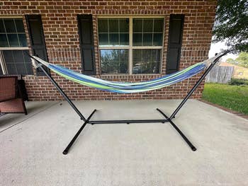 Hammock on a metal stand set up on a patio in front of a brick house with large windows. Ideal for outdoor relaxation