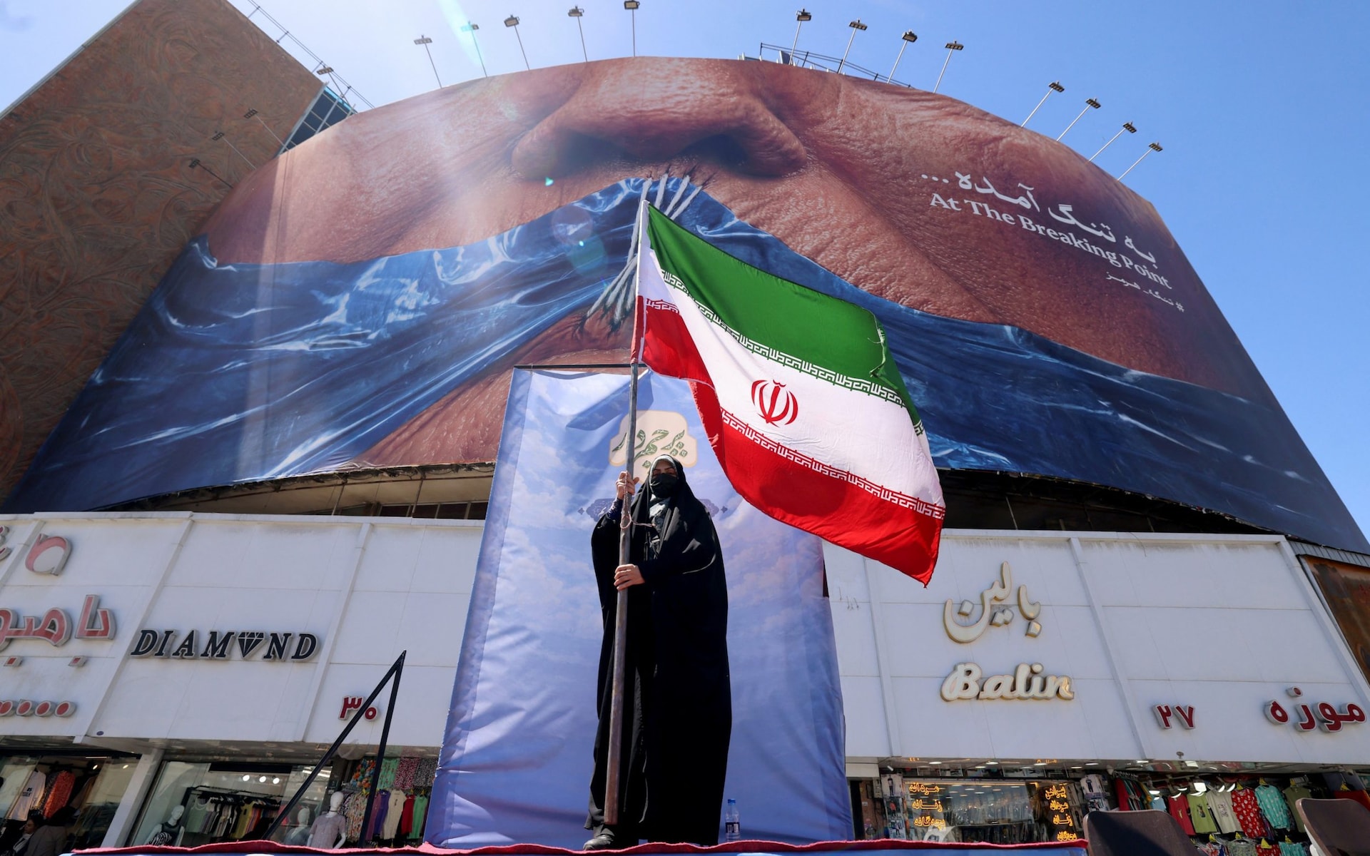 A woman holds the Iranian flag as she stands infront of an anti-US billboard referring to President Donald Trump and the Strait of Hormuz, installed on a building at the Valiasr Square in Tehran on May 10, 2026