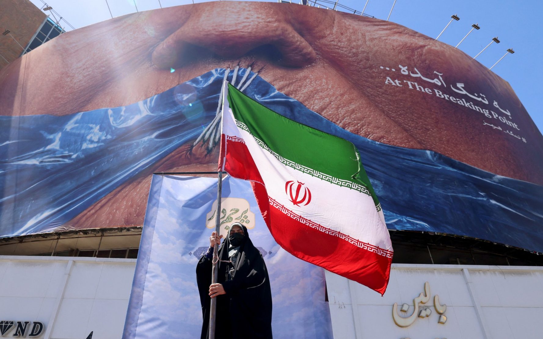 A woman holds the Iranian flag as she stands infront of an anti-US billboard referring to President Donald Trump and the Strait of Hormuz, installed on a building at the Valiasr Square in Tehran on May 10, 2026