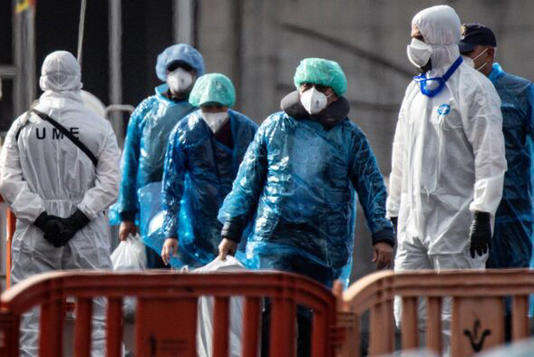 A group of individuals dressed in personal protective equipment, including masks and gloves, are walking together in an outdoor 