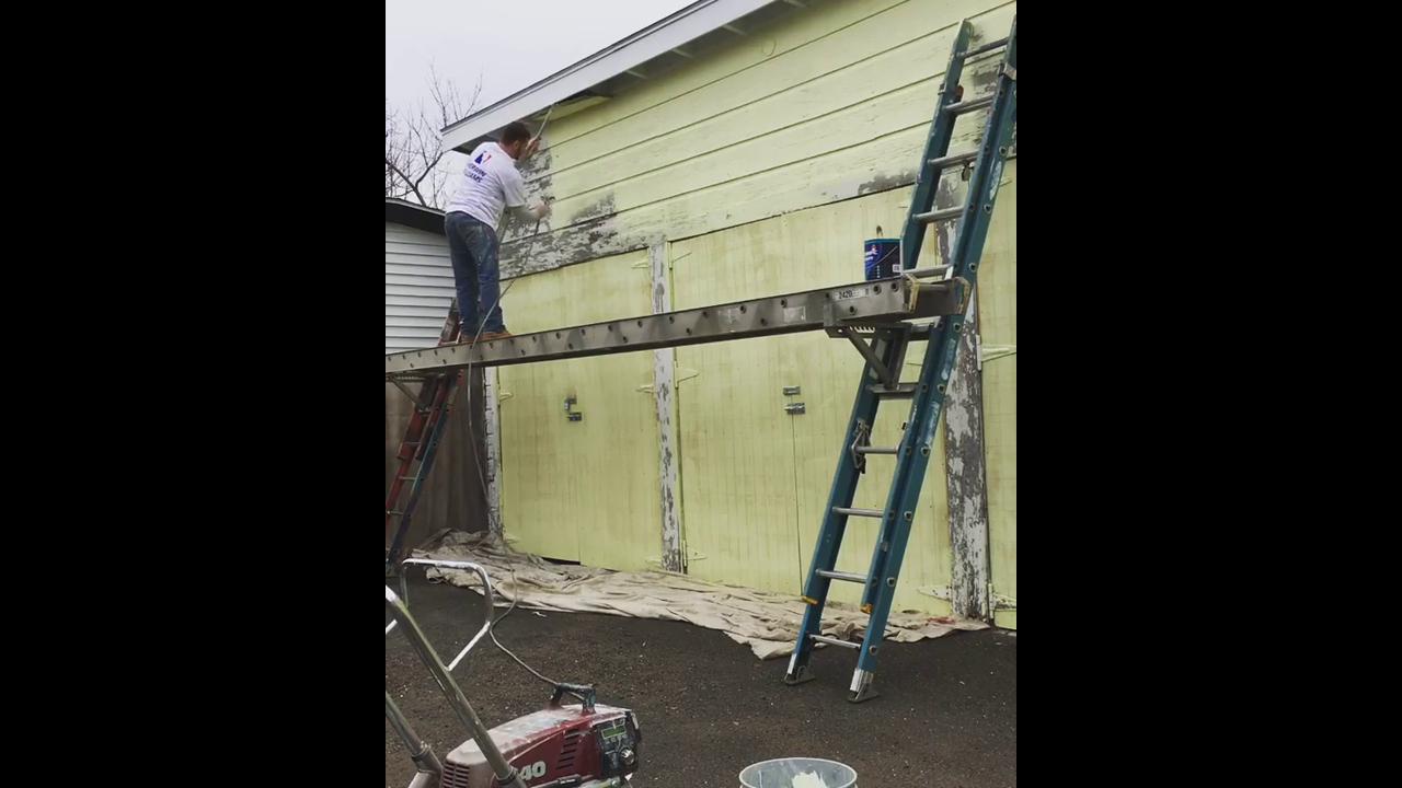 Removing old exterior paint with scraper tool creating clean wall surface