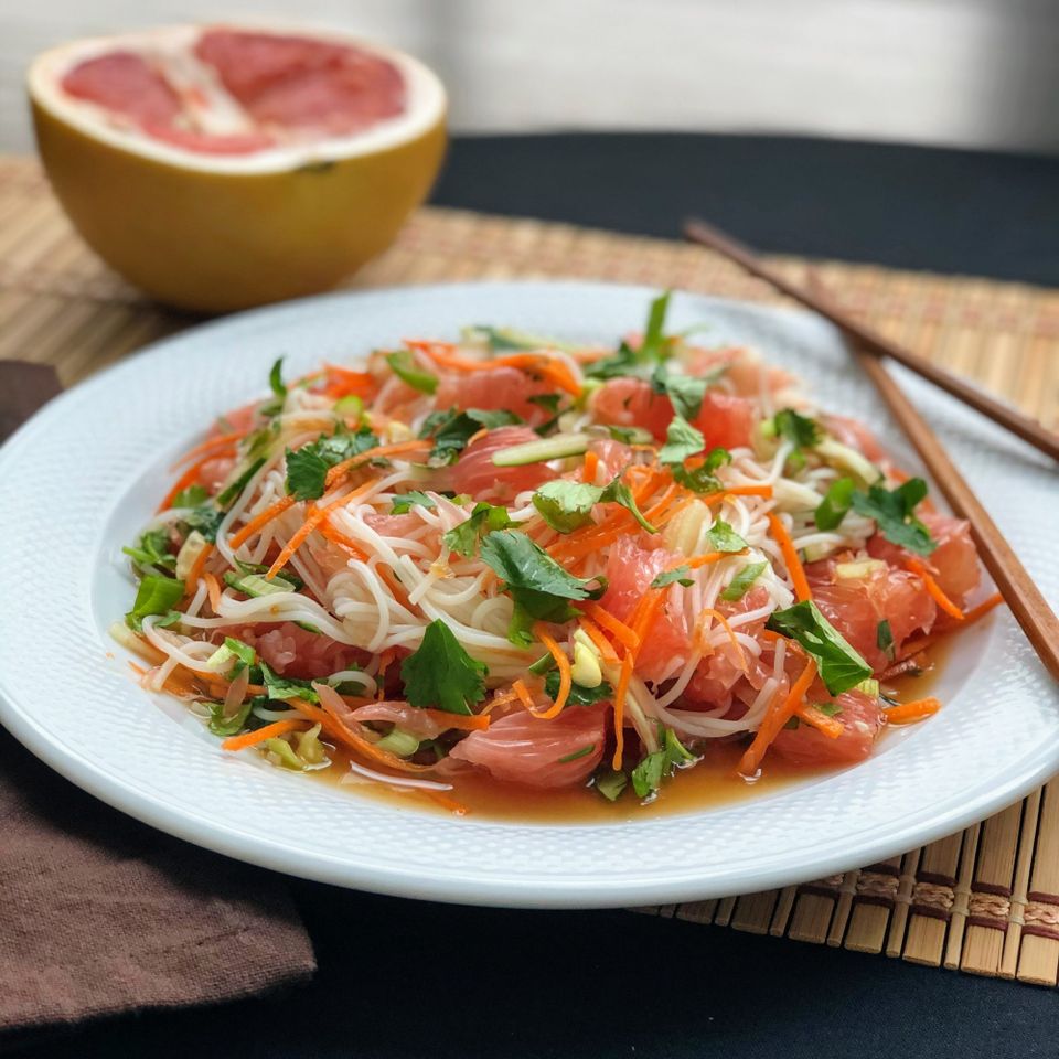 a white bowl filled with a colorful salad, with half a pomelo in the background