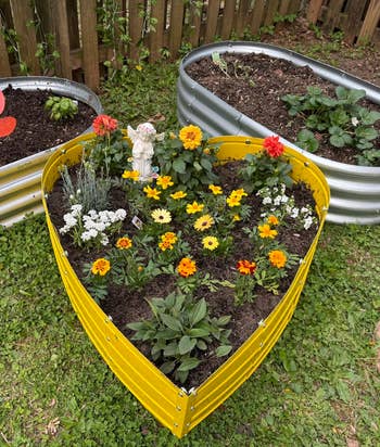 Three metal raised garden beds full of various blooming flowers and small plants on a grassy yard, enhancing outdoor gardening decor