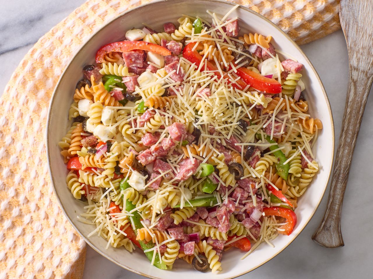 A bowl of Italian pasta salad with various ingredients and shredded cheese on top