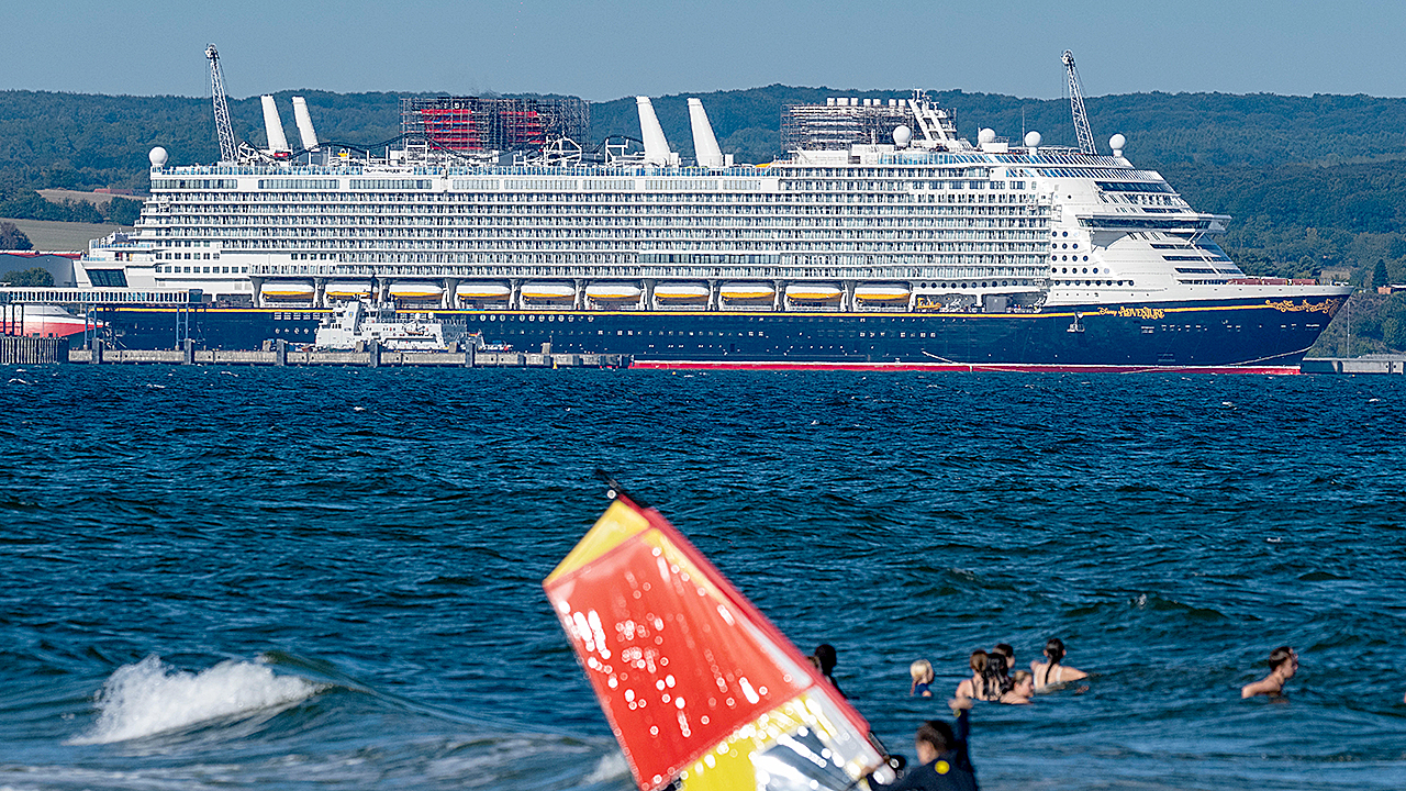 The cruise ship "Disney Adventure", built in the Wismar shipyard, is moored in the port of Mukran on the island of Rügen, while bathers and a windsurfer are in the water in the foreground. After around seven years of construction, one of the world's largest cruise ships starts its test voyages. The US shipping company Disney Cruise Line took over the ship from the insolvency estate and is having it built by the Meyer shipyard in Papenburg, Lower Saxony. The ship will be in service for the Disney Group in Southeast Asia from the end of 2025.