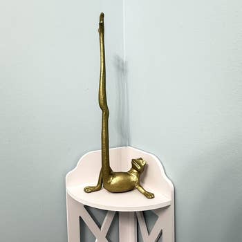 A gold cat-shaped doorstop with an elongated tail rests on a white corner shelf