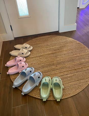 Three pairs of dinosaur-themed slippers are arranged on a round rug by a doorway, showcasing cozy at-home footwear options
