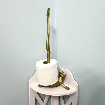 Toilet paper holder shaped like a frog with an extended leg, holding a roll. Decorative and functional home accessory