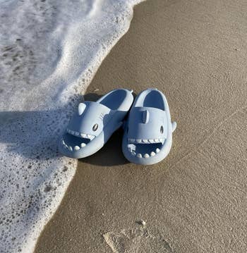 Shark-themed clogs on a sandy beach with gentle waves washing over them