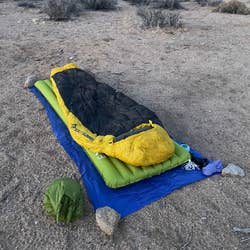 Sleeping bag and mat setup on a desert landscape with mountains in the background, suitable for outdoor camping