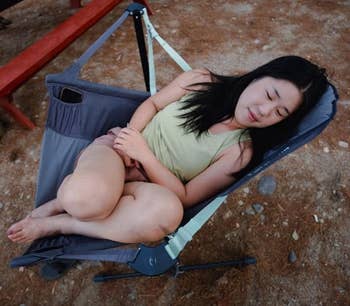 Person comfortably napping in a portable camping chair outdoors, showcasing its compact and supportive design for relaxation in nature settings