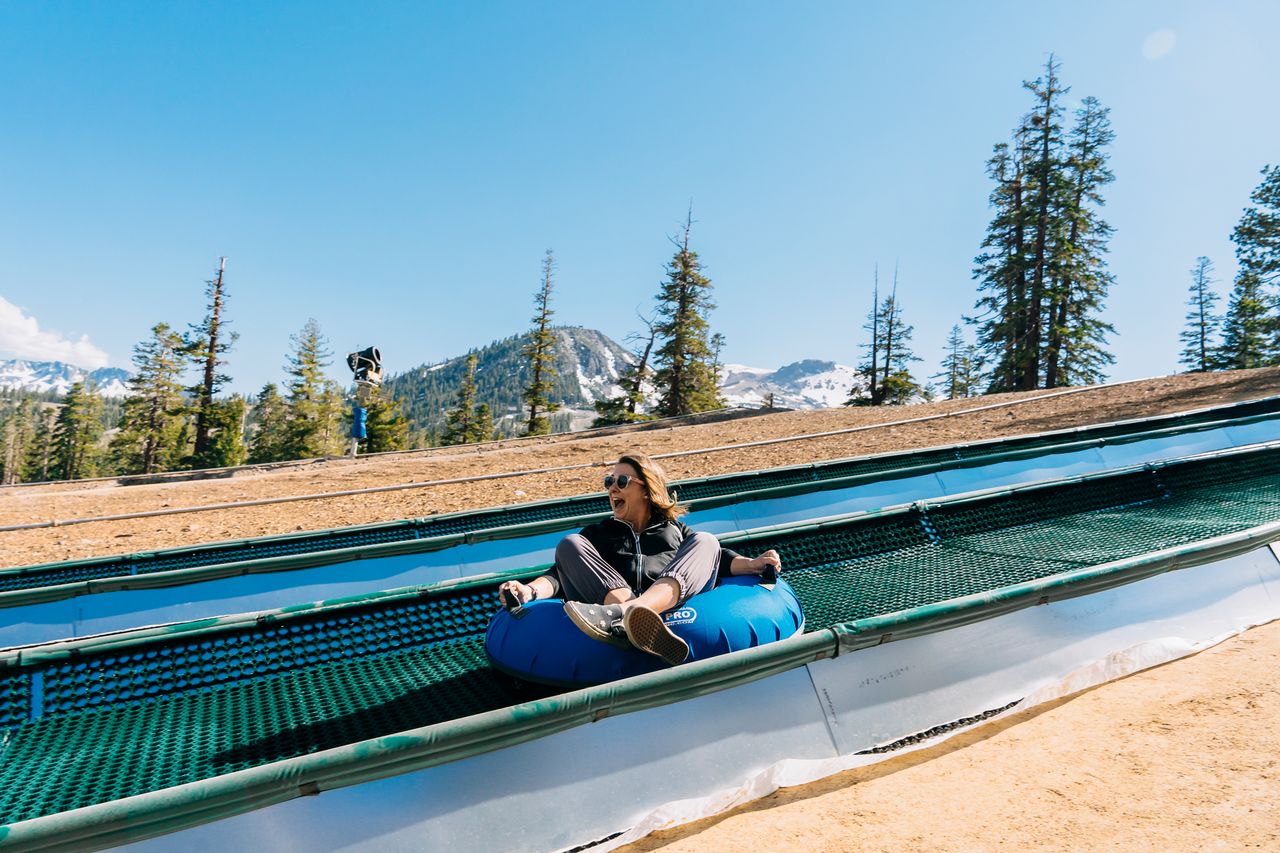 Person on an inflatable snow tube in a mountainous outdoor setting with trees in the background