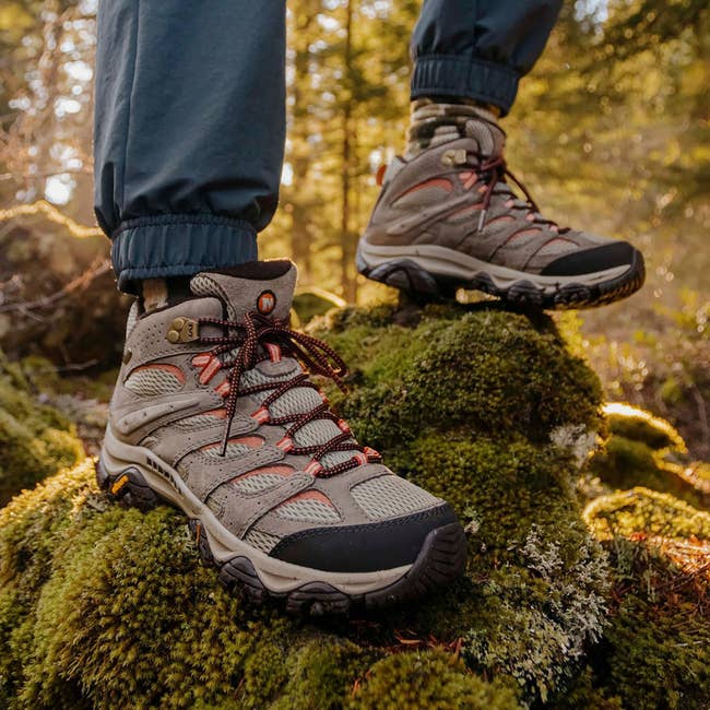 Person wearing rugged hiking boots standing on mossy rocks in a forest setting