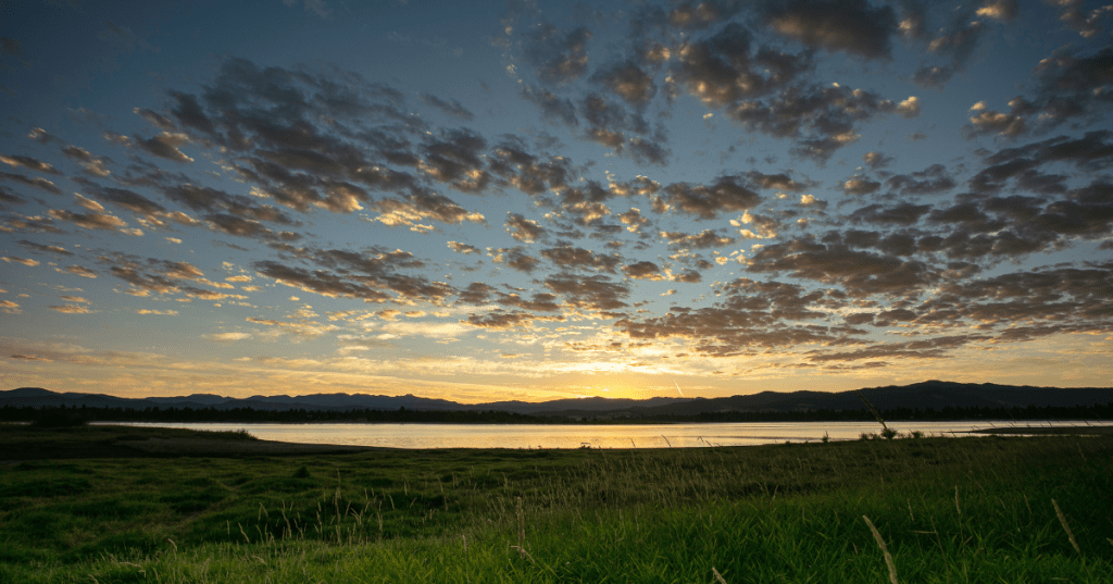A scenic view of Lake Cascade in central Idaho at sunrise, with a colorful sky filled with clouds and mountains in the background.