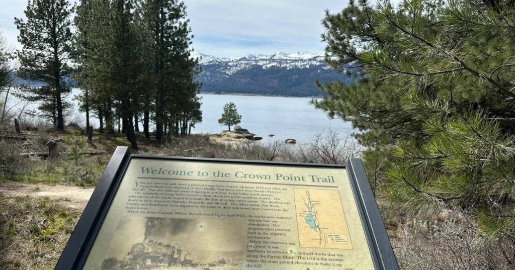 Information sign for the Crown Point Trail near Lake Cascade with water and mountains in the background, surrounded by trees.